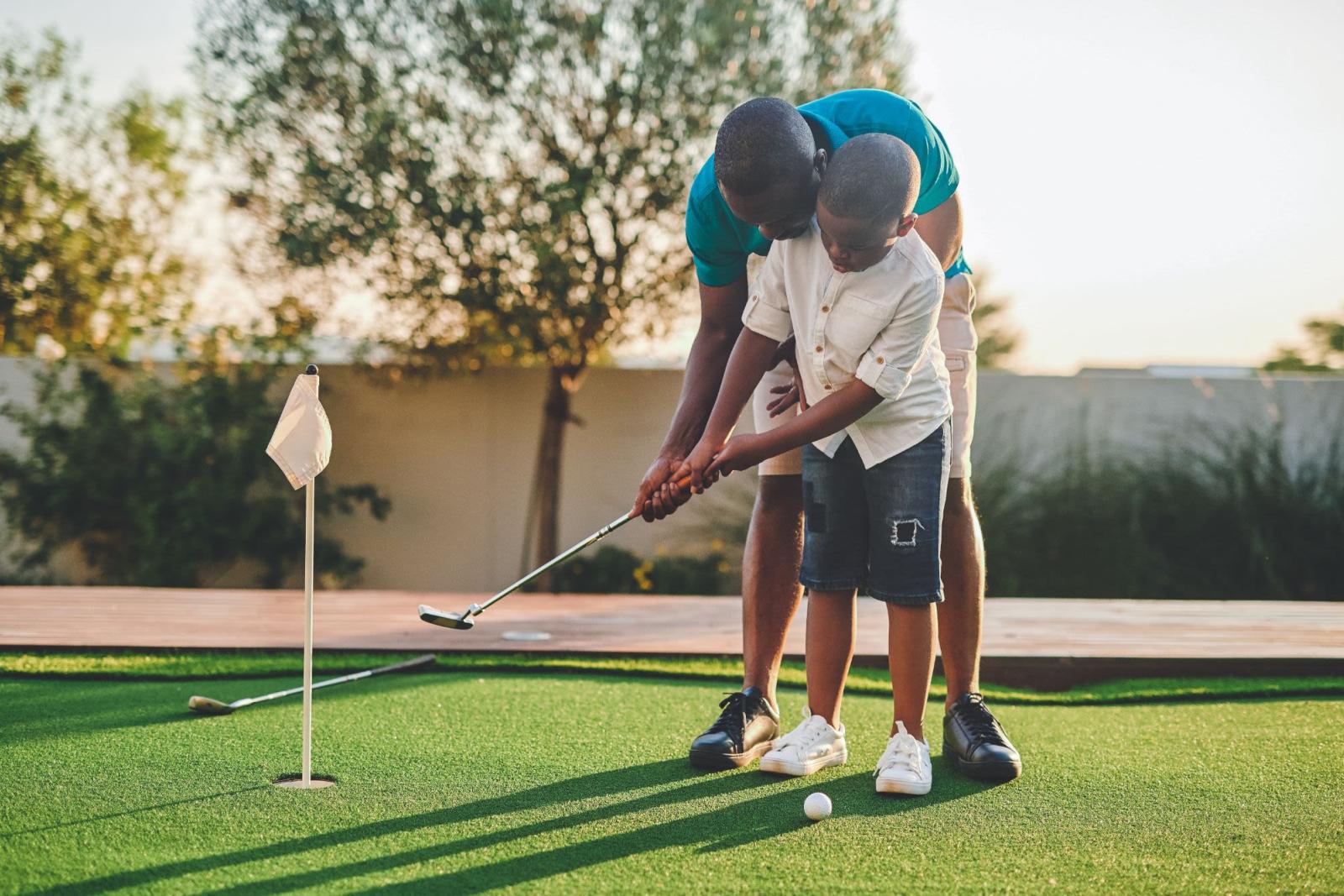 A man teaches his son how to golf