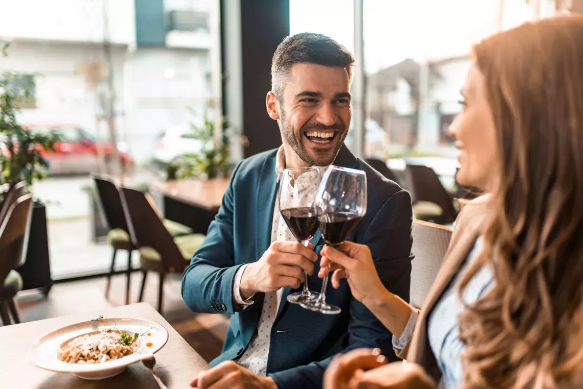 A man and woman clink their wine glasses at a restaraunt