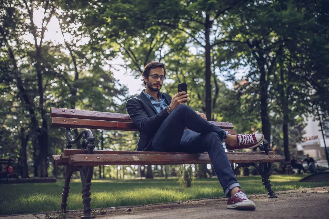 Man sitting on park bench while looking at phone