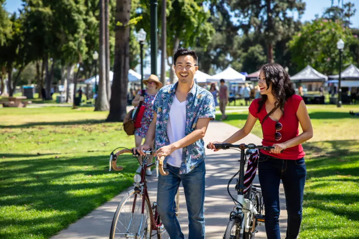 Man and woman walking their bikes through a park