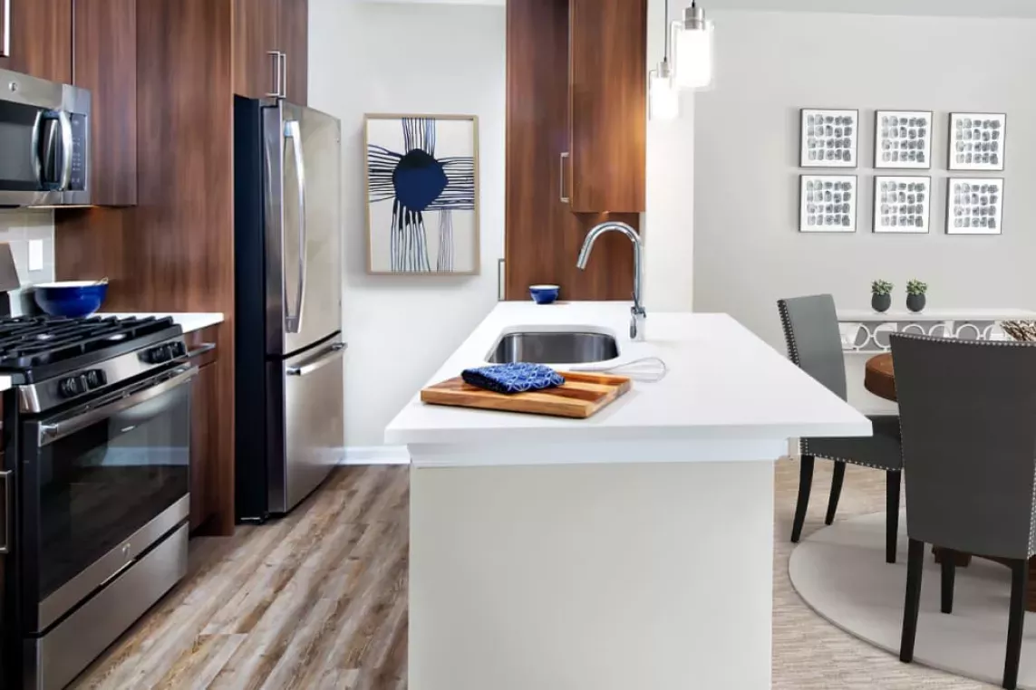 A contemporary kitchen with stainless steel appliances, wood cabinetry, and a quartz countertop island, leading into a stylish dining area.