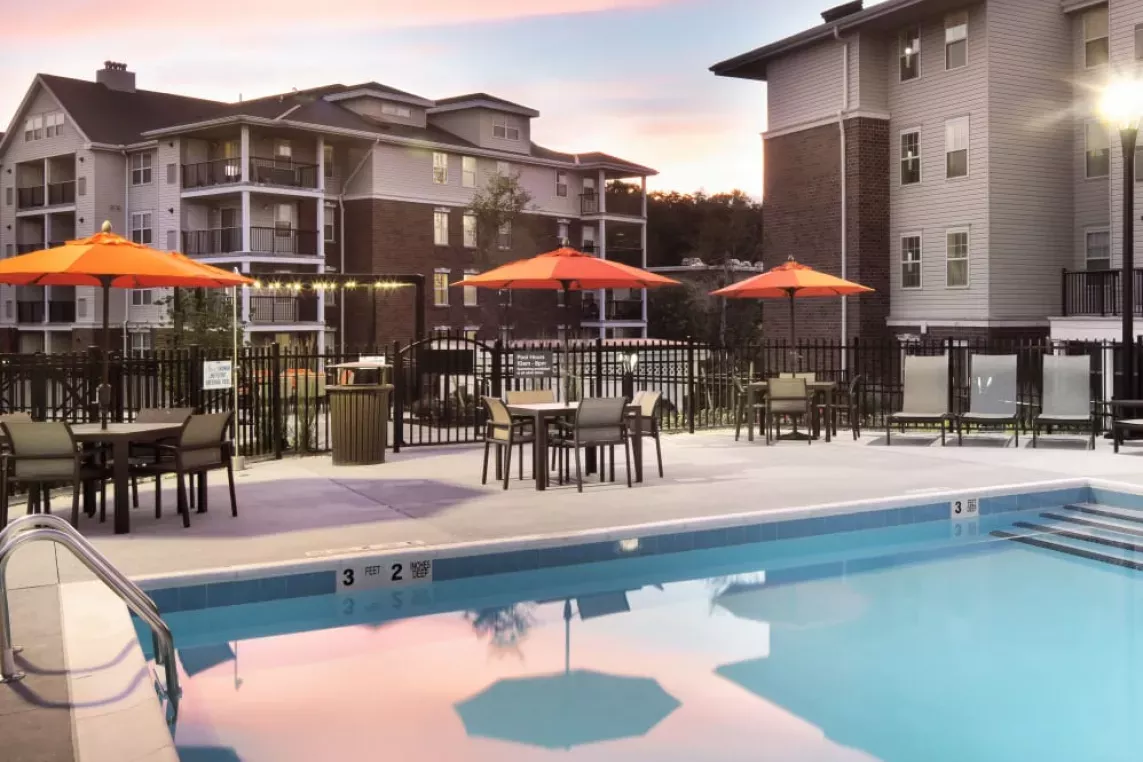 A stunning sunset over the pool area, reflecting soft colors in the water, with orange umbrellas and lounge chairs for relaxation.
