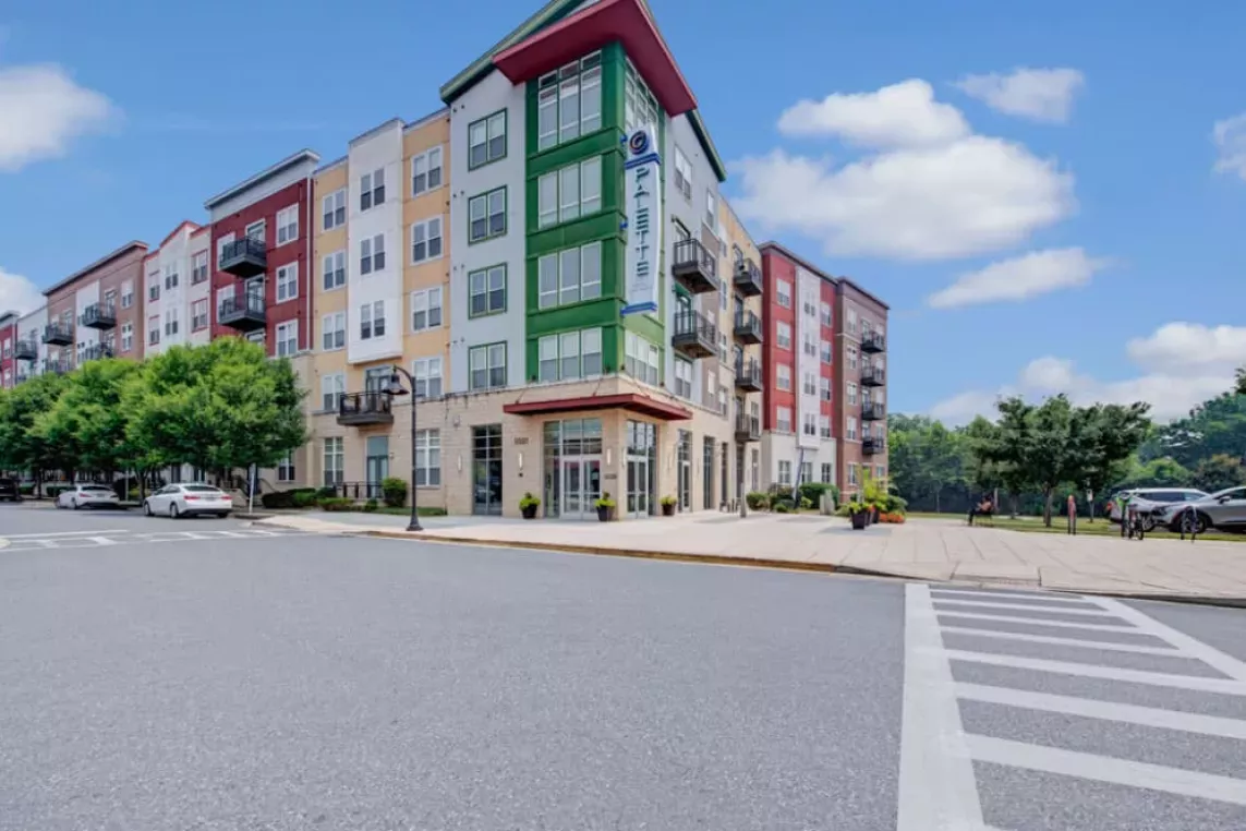 The exterior view of a colorful multi-story apartment building with landscaped sidewalks and a corner entrance.