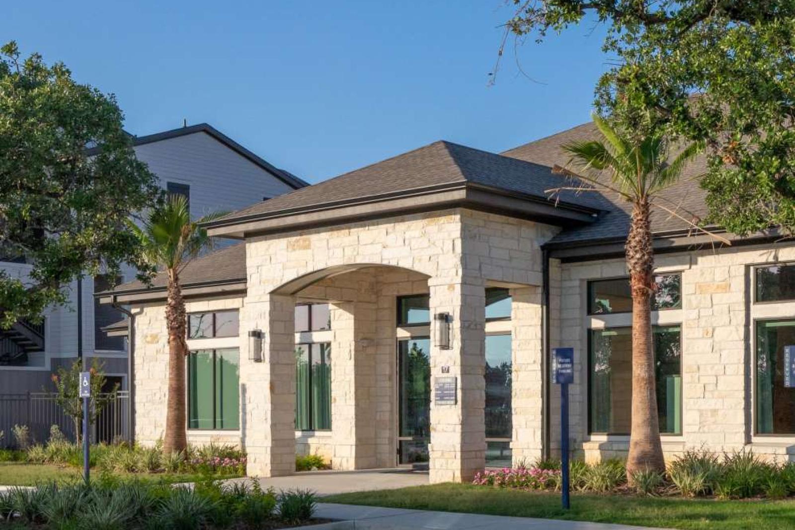Grand clubhouse exterior with stone-accented architecture, lush landscaping, and a welcoming entrance that sets the tone for luxury living.