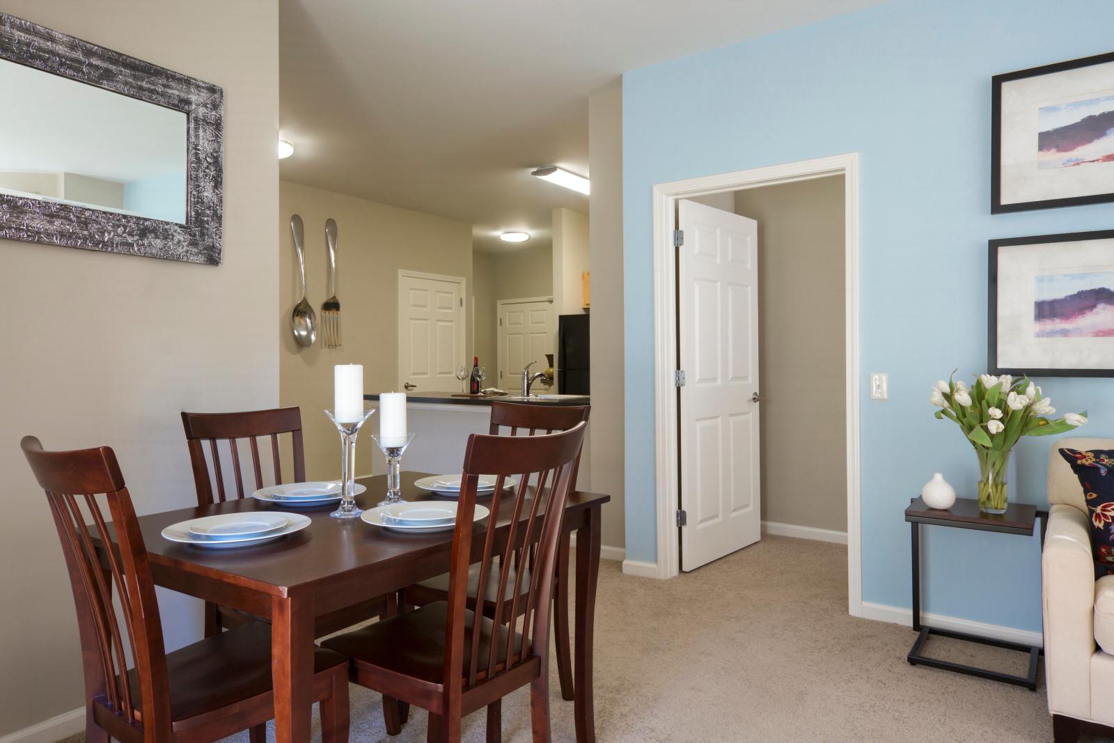 The dining area at Oak Enclave Luxury Apartments features a stylish wooden table set for four, with an open-concept design leading into a modern kitchen. Soft lighting, elegant decor, and a cozy ambiance create the perfect space for dining and entertaining.