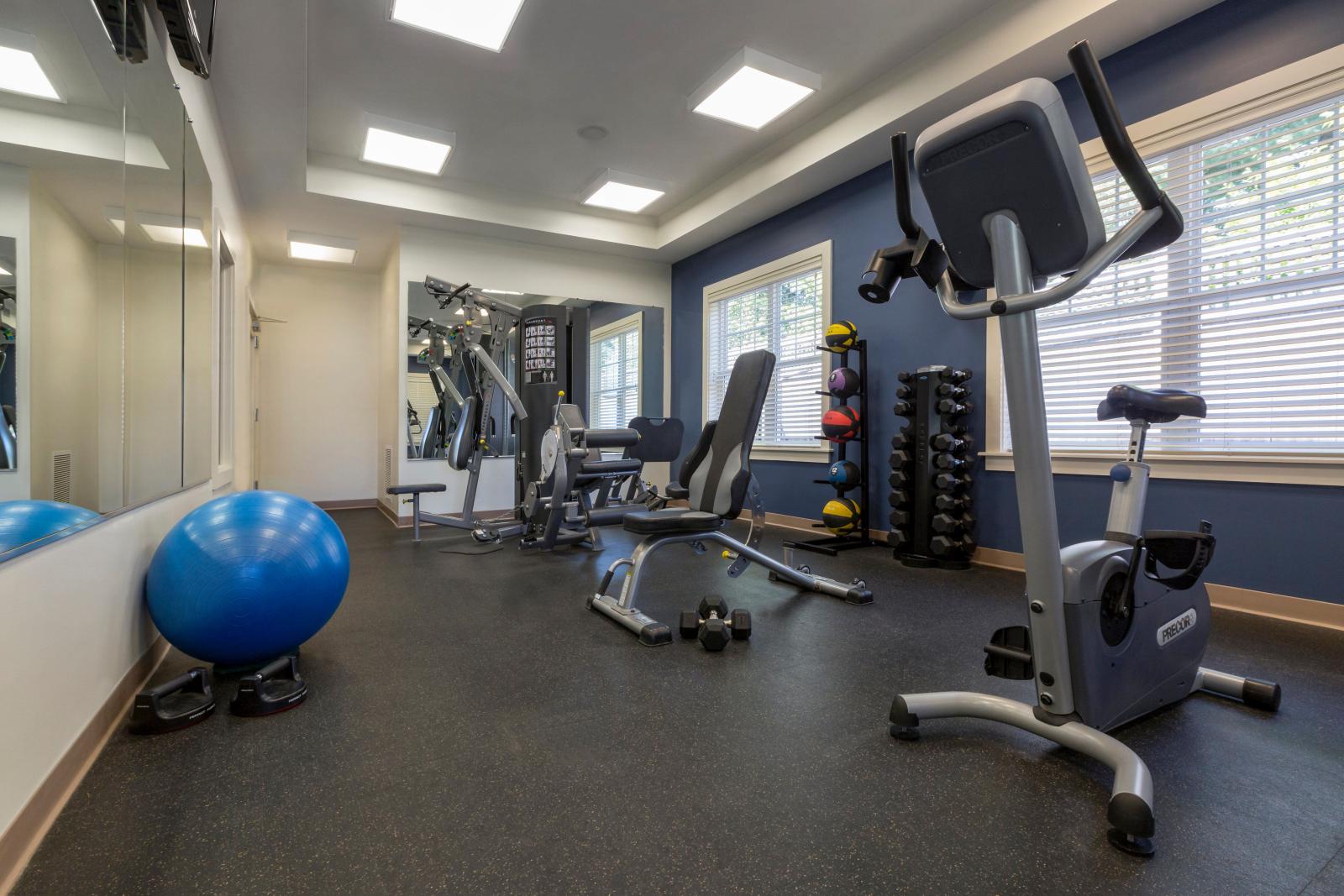 The state-of-the-art fitness center at Oak Enclave Luxury Apartments features a variety of workout equipment, including cardio machines, strength training stations, free weights, and medicine balls. Large windows provide ample natural light, creating a bright and inviting exercise space for residents.