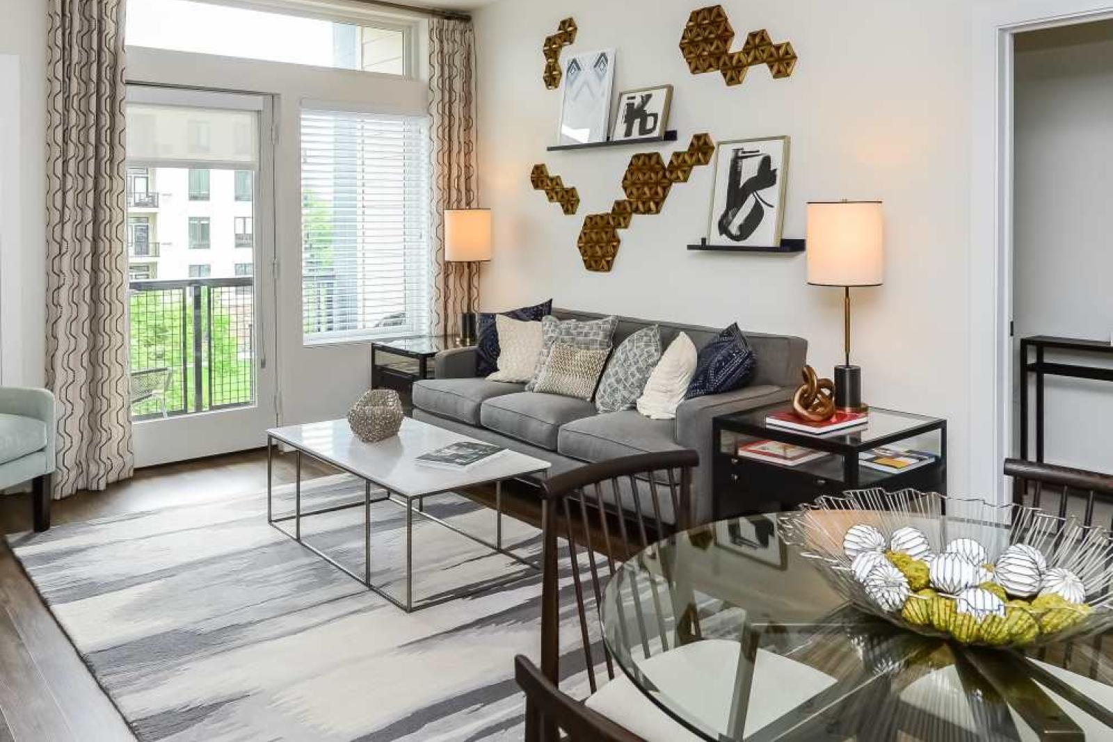 Contemporary living room featuring a gray sofa, modern wall art, and large windows leading to a private balcony with natural light.
