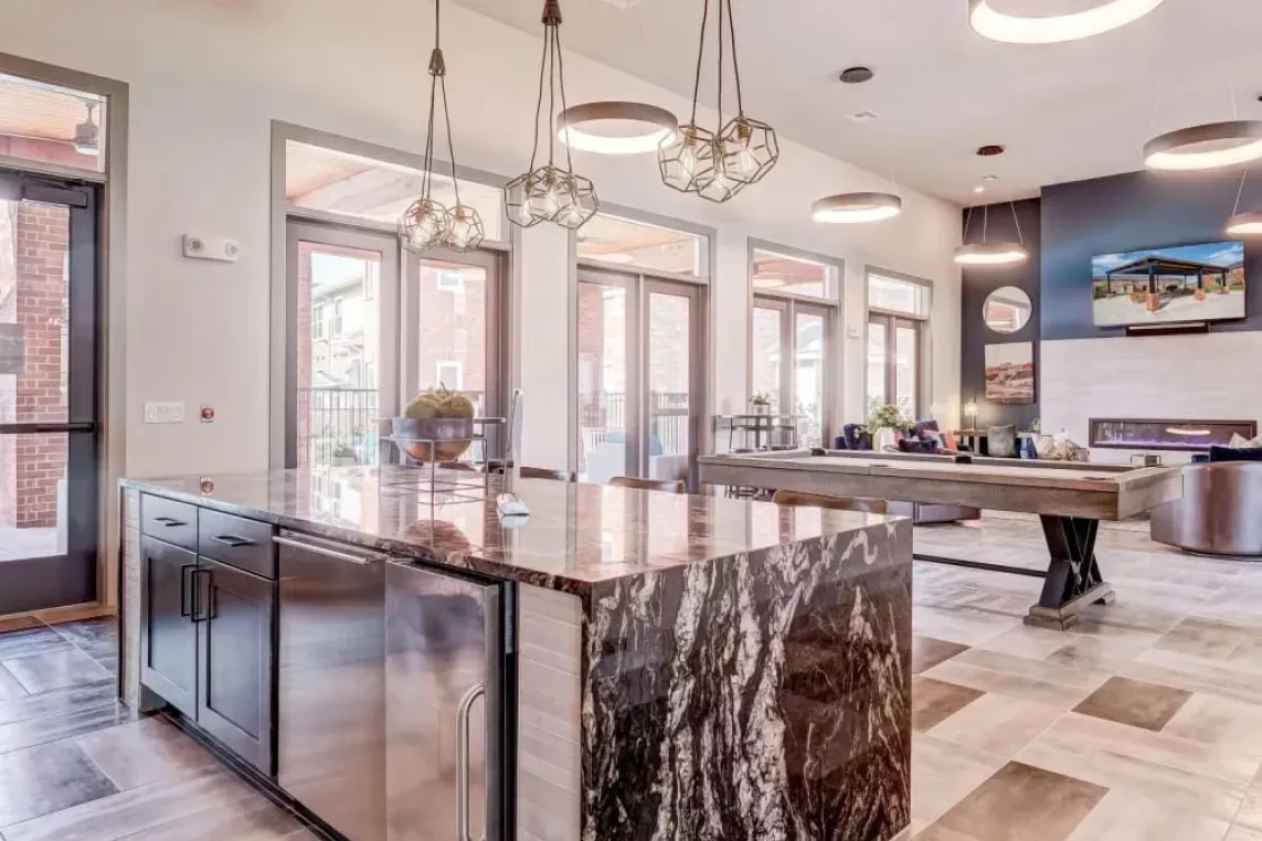 Elegant clubhouse kitchen with a luxurious marble island, modern lighting, and access to the community lounge at The Emerson at Forney Luxury Apartments.