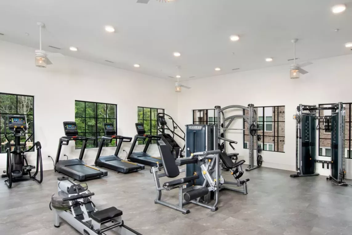 A well-equipped fitness center with treadmills, strength machines, and natural light from large windows.