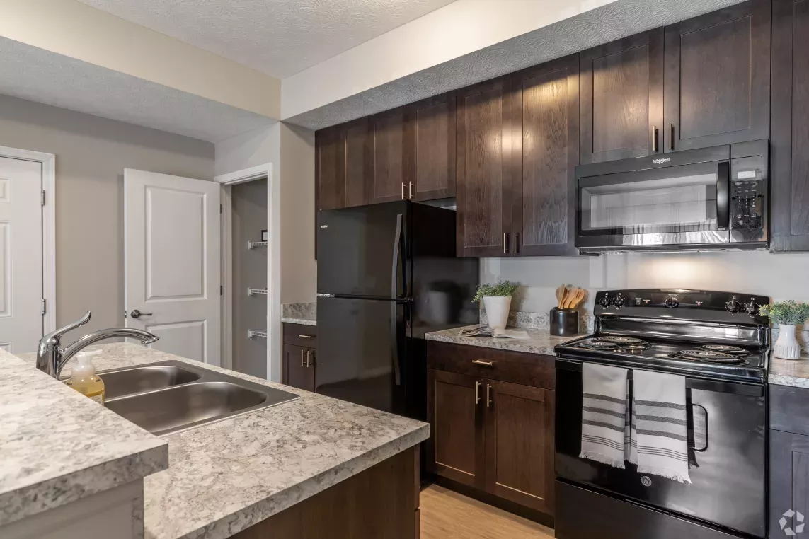 A modern kitchen with dark wood cabinetry, granite countertops, and a double sink at Victoria Manor Luxury Apartments.