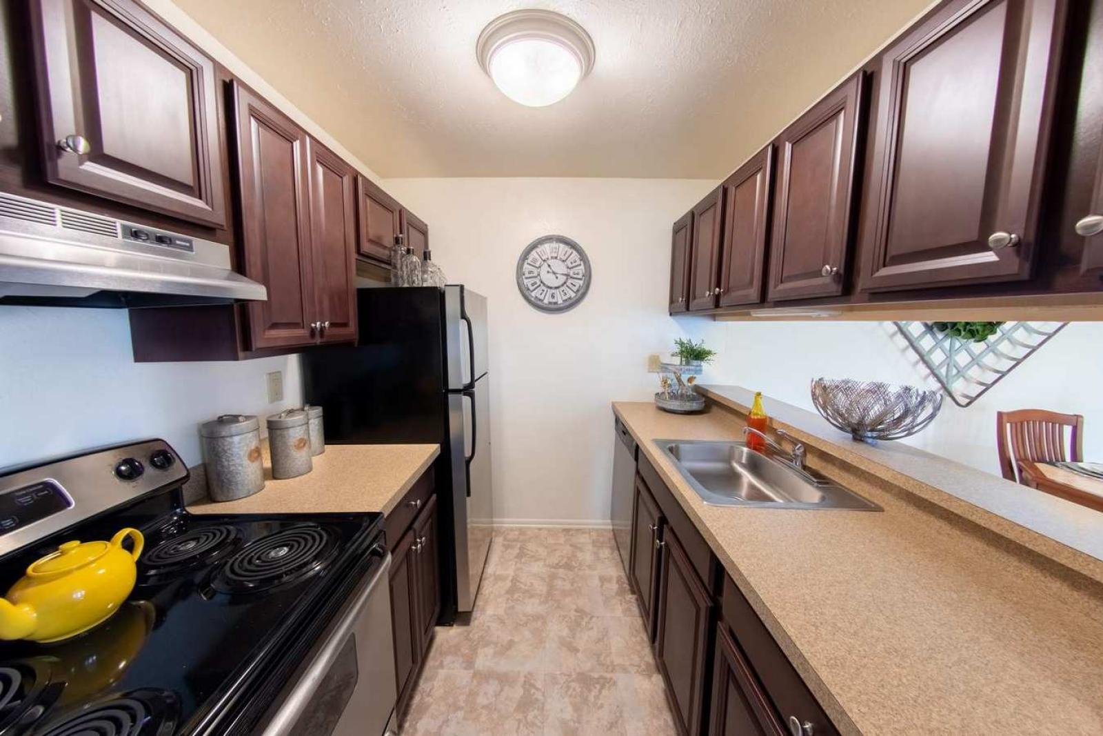 Well-equipped kitchen with sleek countertops, stainless steel appliances, and classic dark wood cabinetry at Forest Creek Apartments