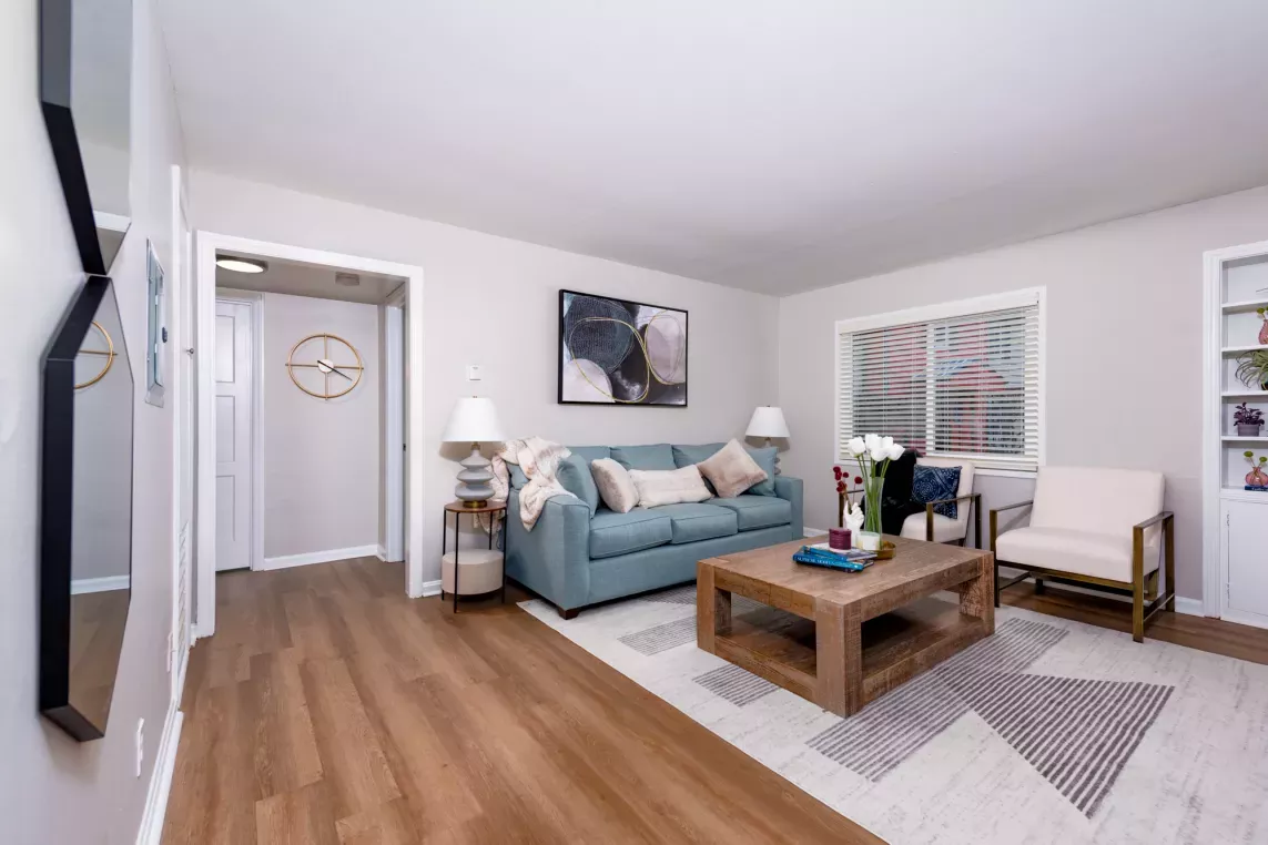 Bright living room with wood-style flooring, a light blue couch, modern artwork, and a large window allowing natural light into the space.