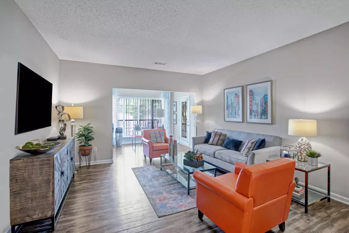 Spacious living room at Amber Chase Apartments with two orange chairs, large sofa, and mounted flat-screen TV.