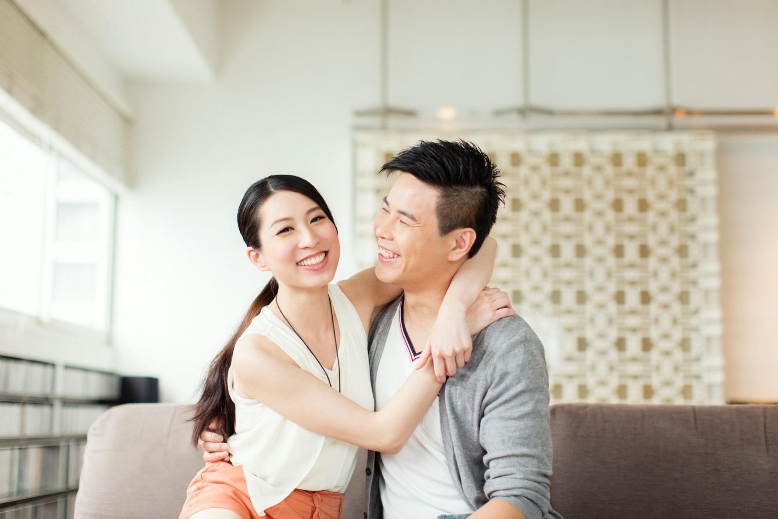 A couple sits on a couch and smiles in a well lit room