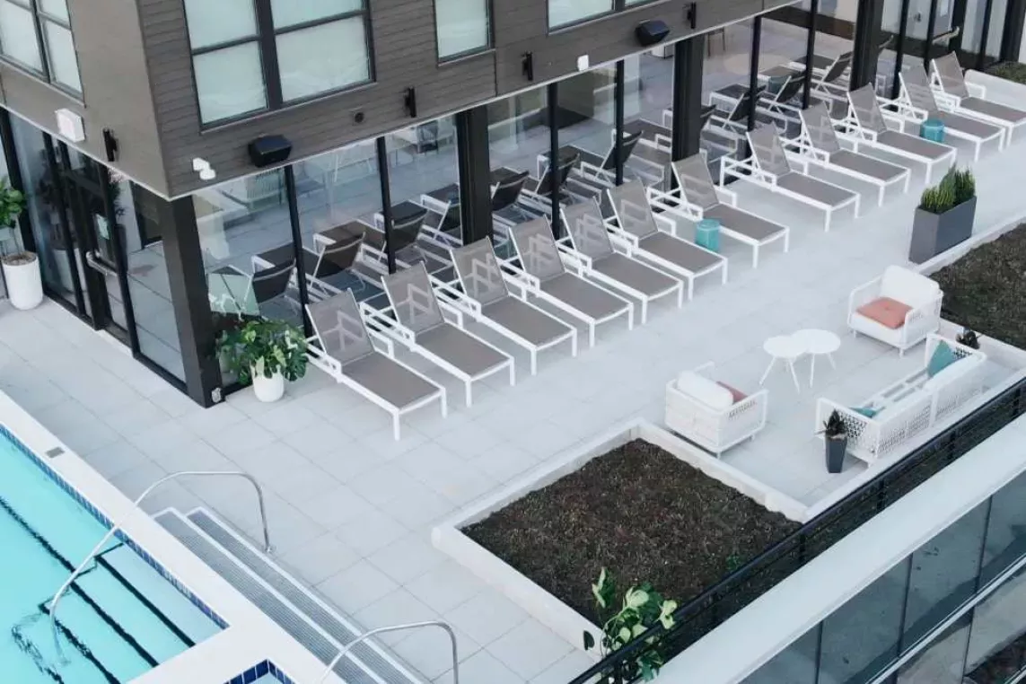 A rooftop pool area at Industry Columbus Apartments featuring a row of modern lounge chairs, cozy outdoor seating, and lush greenery, creating a stylish and relaxing retreat for residents.