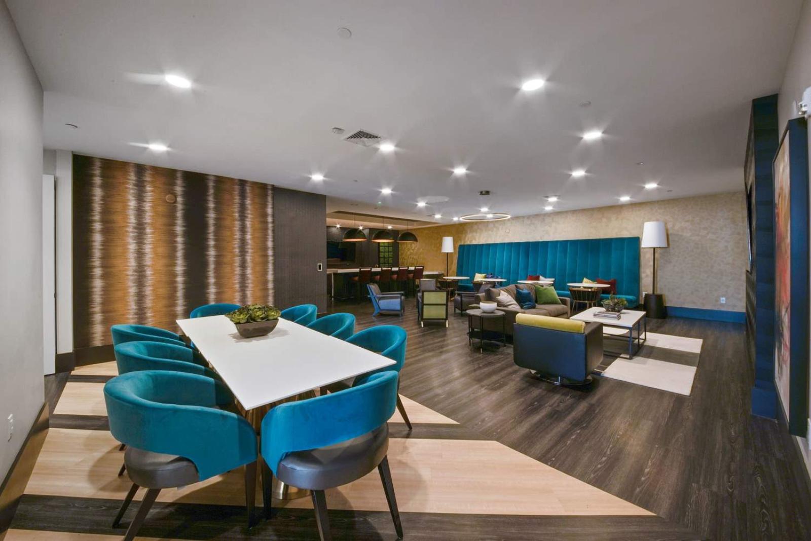 A cozy communal area with plush teal chairs, a large dining table, and warm lighting.