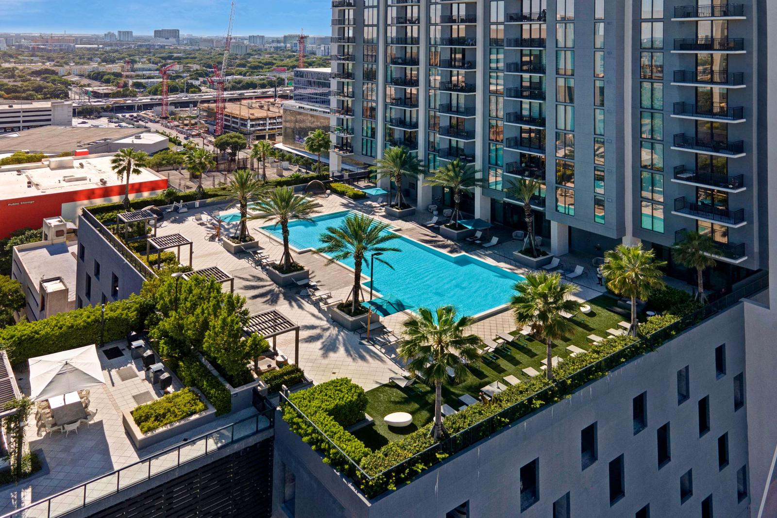 A stunning rooftop pool deck crowns the Parkline Miami tower, featuring a large resort-style pool surrounded by lush palm trees, shaded lounge areas, and cozy seating alcoves. Elevated above the city, this vibrant oasis offers panoramic views of the Miami skyline and creates the perfect retreat for urban relaxation.