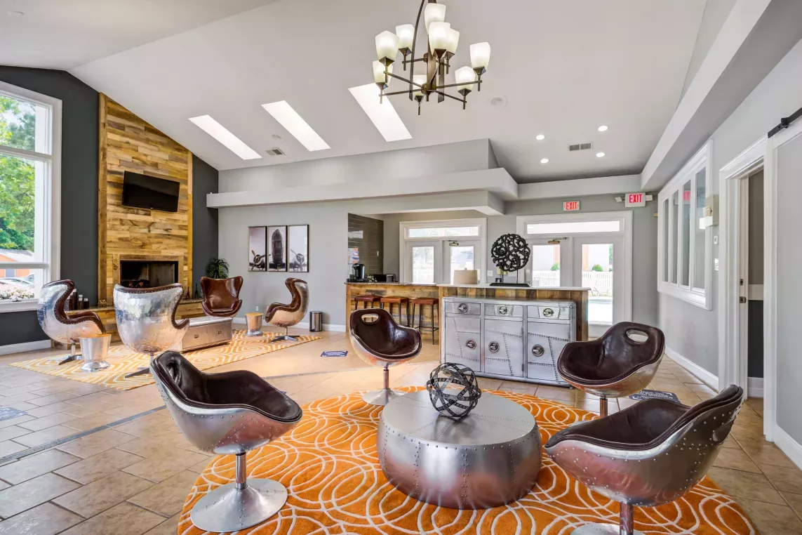 Resident lounge at The Samuel featuring modern aviation-inspired seating, orange patterned rugs, and a rustic wood accent wall with a mounted TV