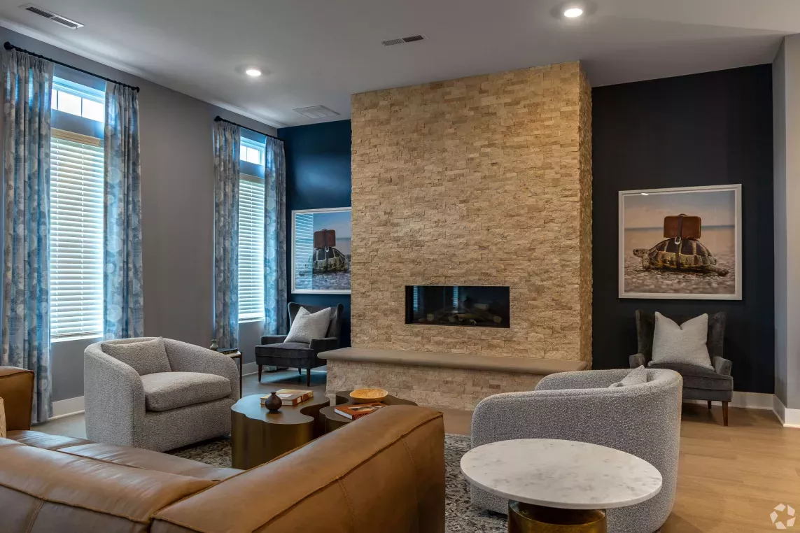 Cozy resident lounge with a floor-to-ceiling stone fireplace, plush seating, and framed turtle artwork on dark accent walls.