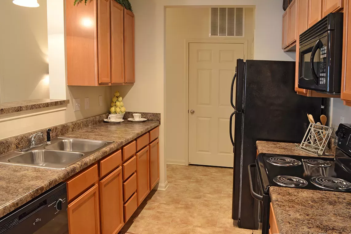 Galley-style kitchen at Market Street Station featuring wood cabinetry, black appliances, and dual sink with granite-look countertops.
