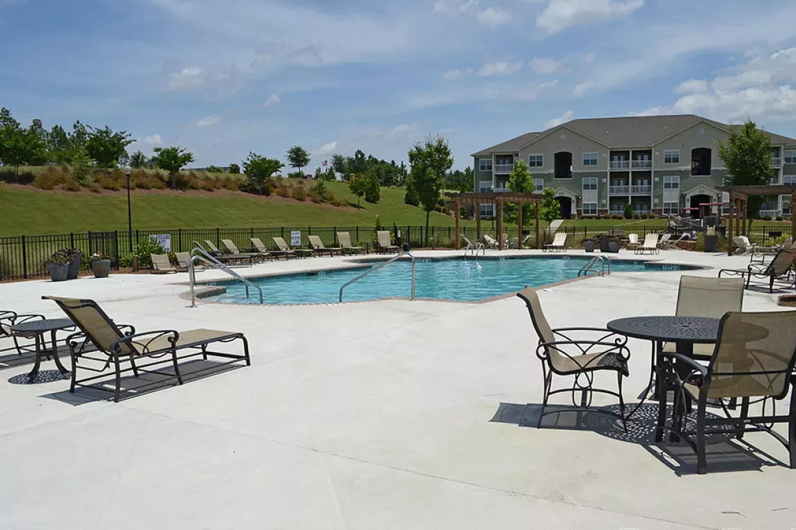 Poolside seating area with lounge chairs and tables, overlooking the swimming pool and landscaped grounds.