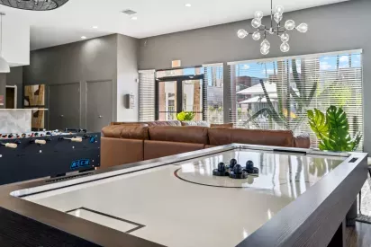 A modern clubhouse at Colter Park featuring an air hockey table, foosball table, stylish leather seating, and large windows with a view of outdoor greenery.