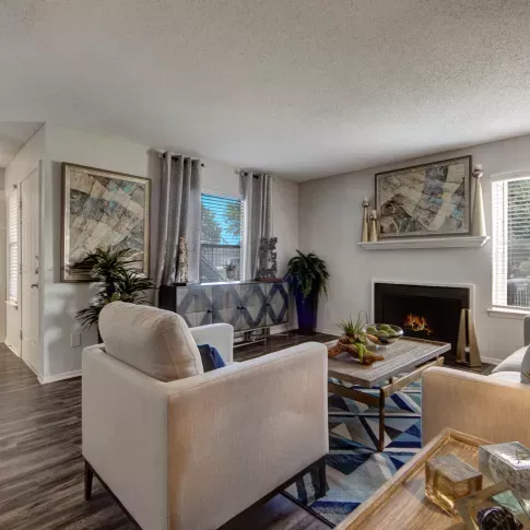 A cozy living room featuring a fireplace, modern furniture, and decorative artwork with natural light streaming through the windows.