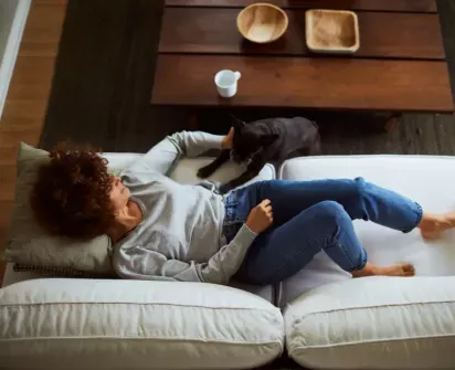  Woman relaxing on a cozy white couch with her dog, enjoying a calm and peaceful moment in a modern, inviting living space.