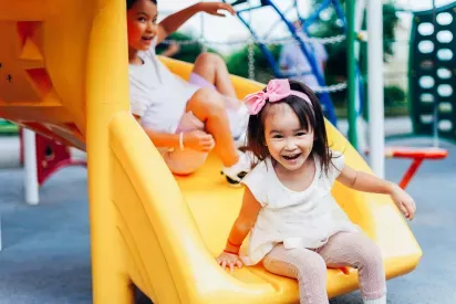 Young children enjoying a bright yellow slide at a playground, with joyful expressions and vibrant play equipment creating a fun and energetic atmosphere.