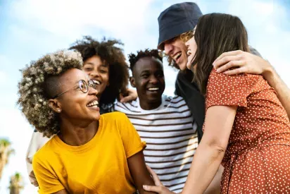  A group of friends laughing and smiling together outdoors under a bright blue sky. The cheerful expressions and warm interactions highlight a sense of community, friendship, and joy.
