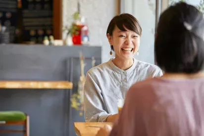 A woman smiling warmly while enjoying a conversation with a friend at a cozy cafe.