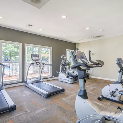  A well-lit fitness center featuring treadmills, stationary bikes, and strength training equipment with large windows overlooking outdoor greenery.