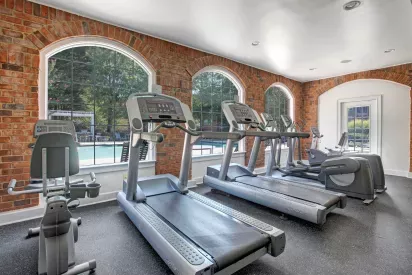 Bright and inviting fitness center with treadmills and exercise equipment, set against large arched windows overlooking an outdoor pool.