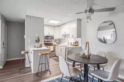 A stylish dining area adjacent to a sleek modern kitchen with white cabinetry, a subway tile backsplash, and natural lighting.