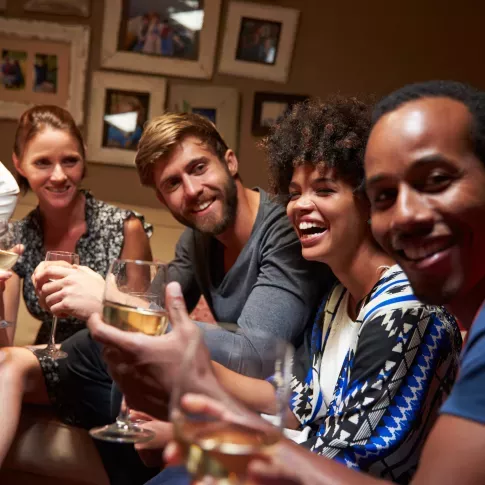 A group of friends enjoying an evening together, laughing and holding glasses of wine in a cozy setting.