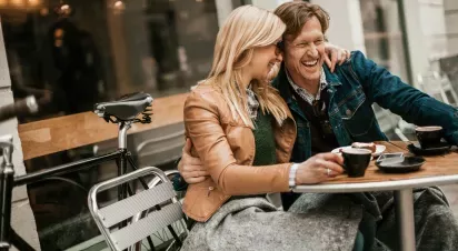  A happy couple sharing a laugh while enjoying coffee and dessert at an outdoor café.