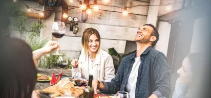 A group of friends enjoying food, wine, and laughter at a cozy outdoor gathering.