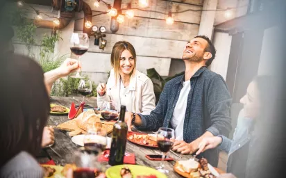 A group of friends enjoying food and wine at an outdoor table decorated with string lights and surrounded by rustic decor.