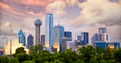 A scenic view of Lewisville, Texas, featuring a vibrant skyline with lush greenery in the foreground and dramatic clouds during sunset.