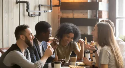 A group of friends enjoying food and coffee together in a cozy indoor setting with warm, rustic decor.