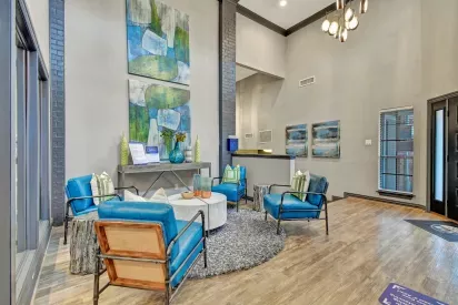 A modern and stylish lounge area featuring blue accent chairs, contemporary artwork, and a cozy round rug in a bright, open space.