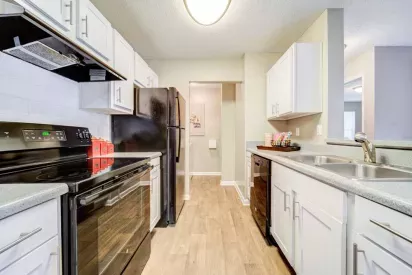 A modern kitchen featuring white cabinetry, black appliances, and a dual-basin sink with wood-style flooring.