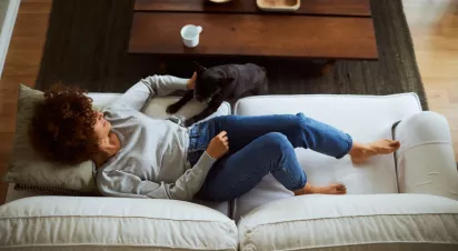  Woman relaxing on a cozy white couch with her dog resting nearby, enjoying a peaceful moment in a warm and inviting living space.