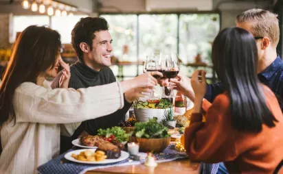 A group of friends toasting with wine glasses over a shared meal at a warmly lit dining table.