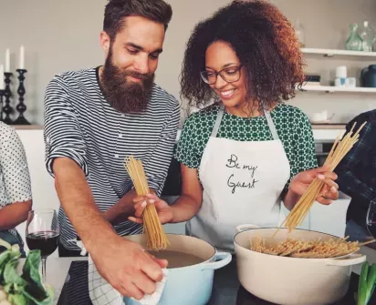 Couple happily cooking together in the kitchen, preparing pasta with smiles and teamwork, creating a warm and inviting atmosphere for home cooking and shared moments.