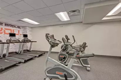 A fitness center with stationary bikes and treadmills arranged under bright overhead lighting.