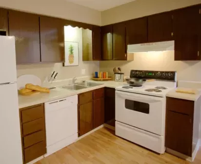 This image showcases a cozy kitchen featuring dark wood cabinetry, a white electric stove, and matching white appliances, complemented by a warm-toned countertop and light wood flooring.
