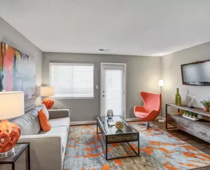 Modern living room with stylish decor, featuring a comfortable sofa with orange accents, a bold orange chair, and a vibrant rug, creating a bright and welcoming atmosphere.