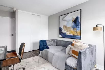 A cozy and modern bedroom featuring a gray upholstered daybed, colorful abstract wall art, and a sleek floor lamp with a gold shade.