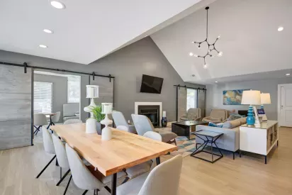 A modern community lounge featuring a long wooden dining table, comfortable seating, a fireplace, and contemporary decor.